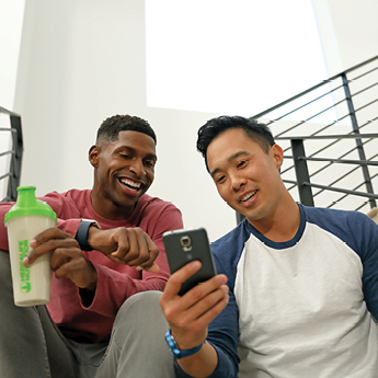 Two Men Looking At A Phone With A Herbalife Nutrition Shake